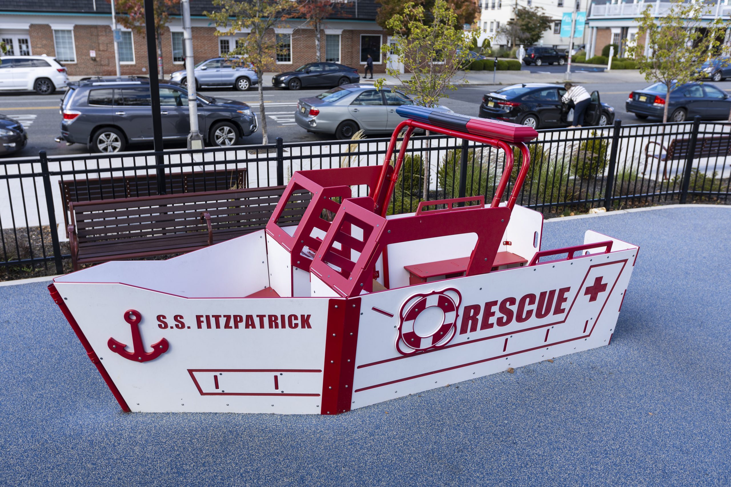 A vibrant red and white commercial rescue boat playhouse for kids on a playground.