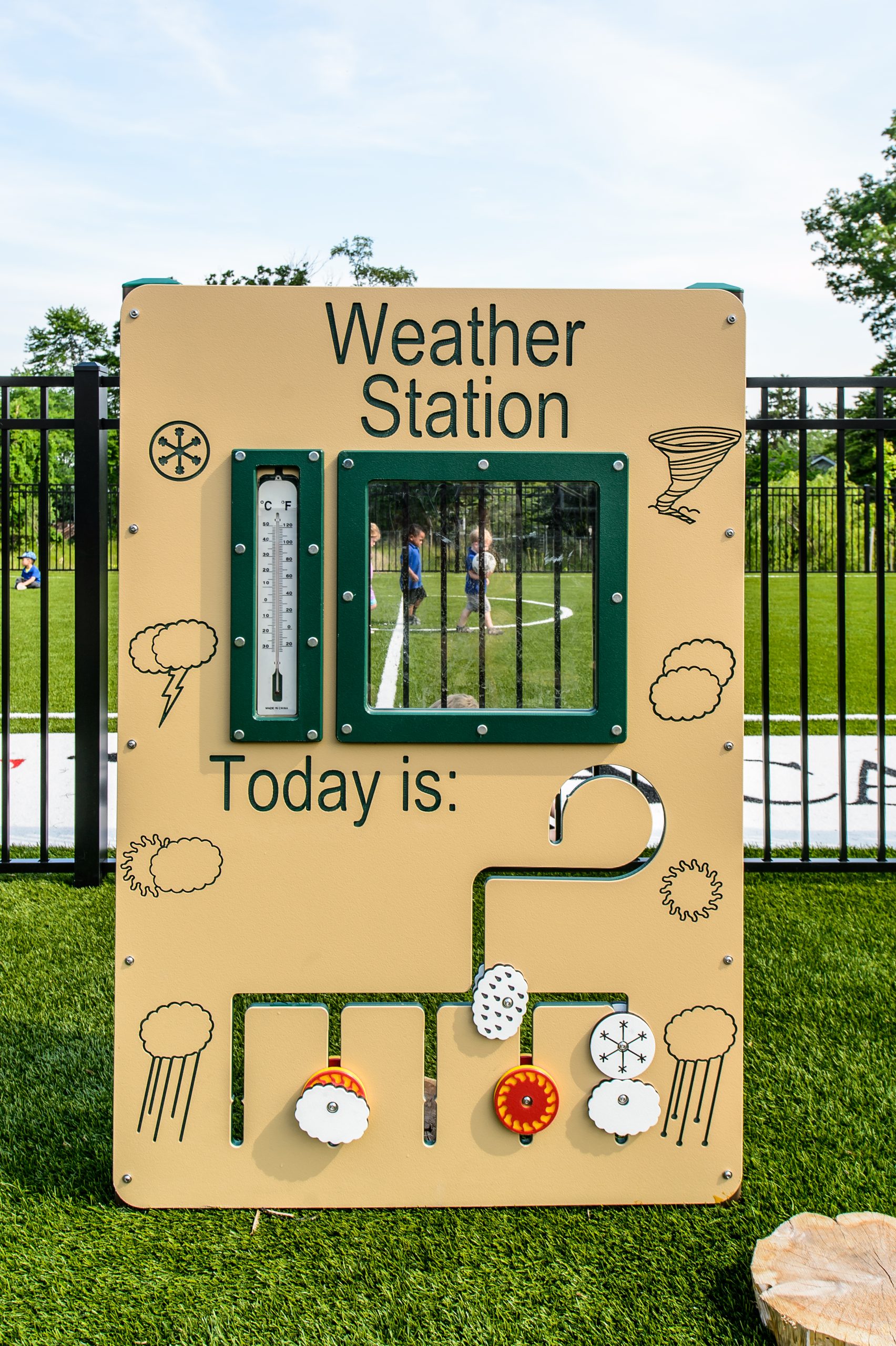 A colorful basic preschool weather station activity panel on a playground, showing a thermometer and weather symbols.