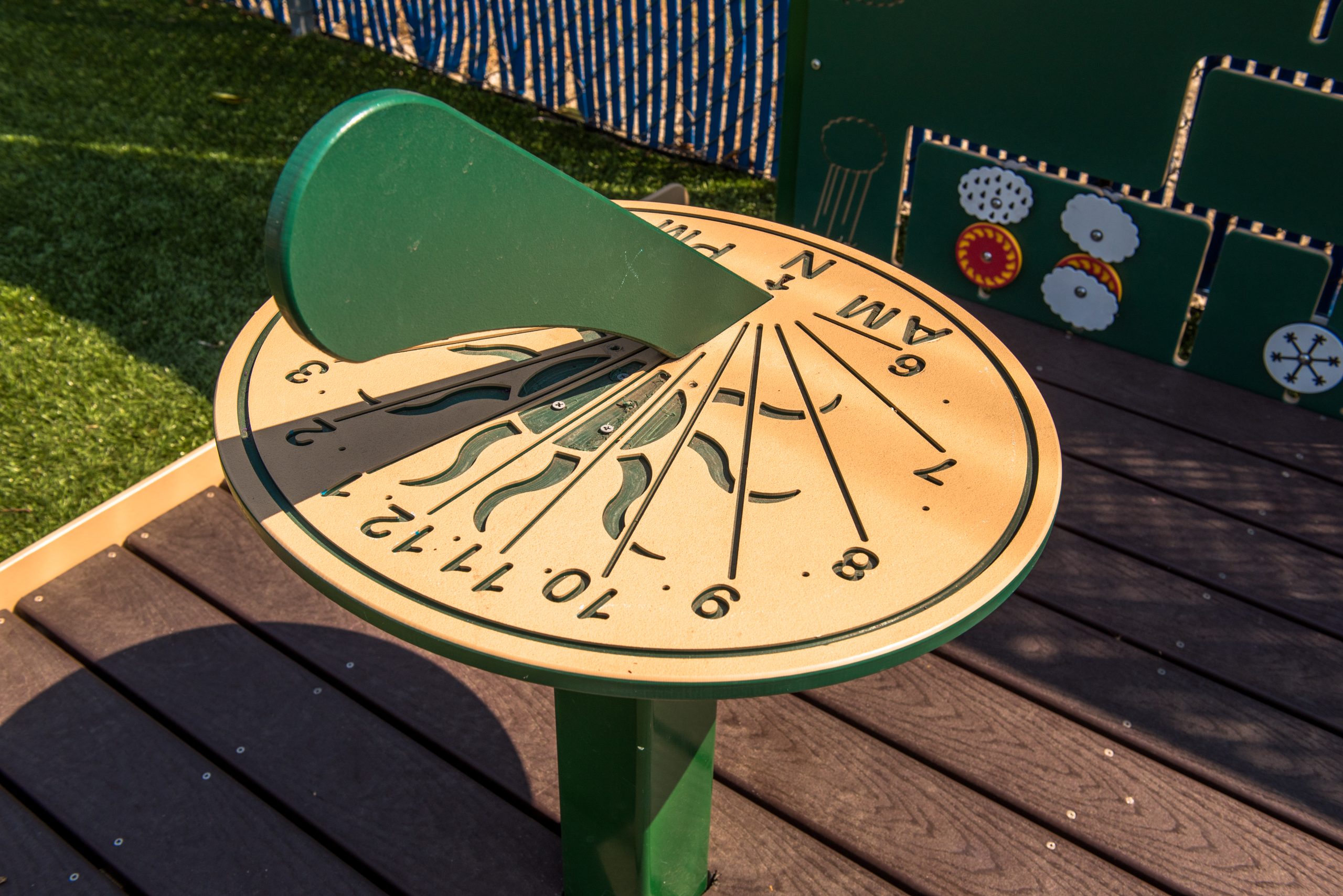 A colorful commercial outdoor sun dial freestanding playground equipment for children aged 2-12, showing bold numbers and a gnomon.